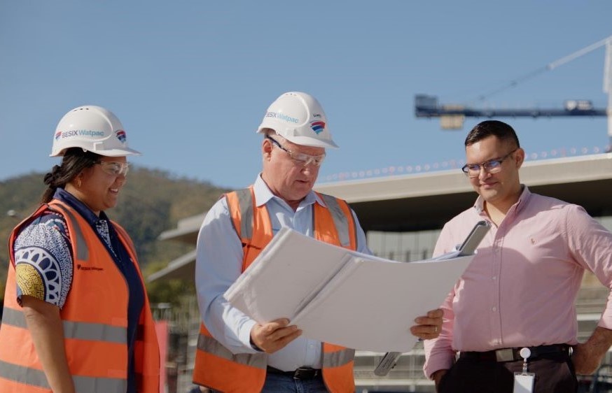 Besix Watpac Project manager and indigenous employee showing plans to NAIF staff with JCU Engineering and Innovation Place construction site and crane in background