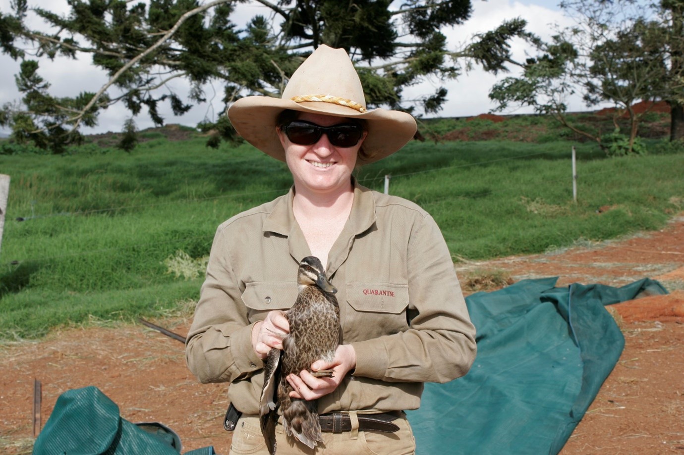 Dr. Beth Cookson in a wide brimmed hat and sunglasses holding a duck