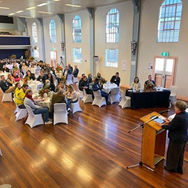 Image of a hall with people sitting at tables and a lectern at the front 