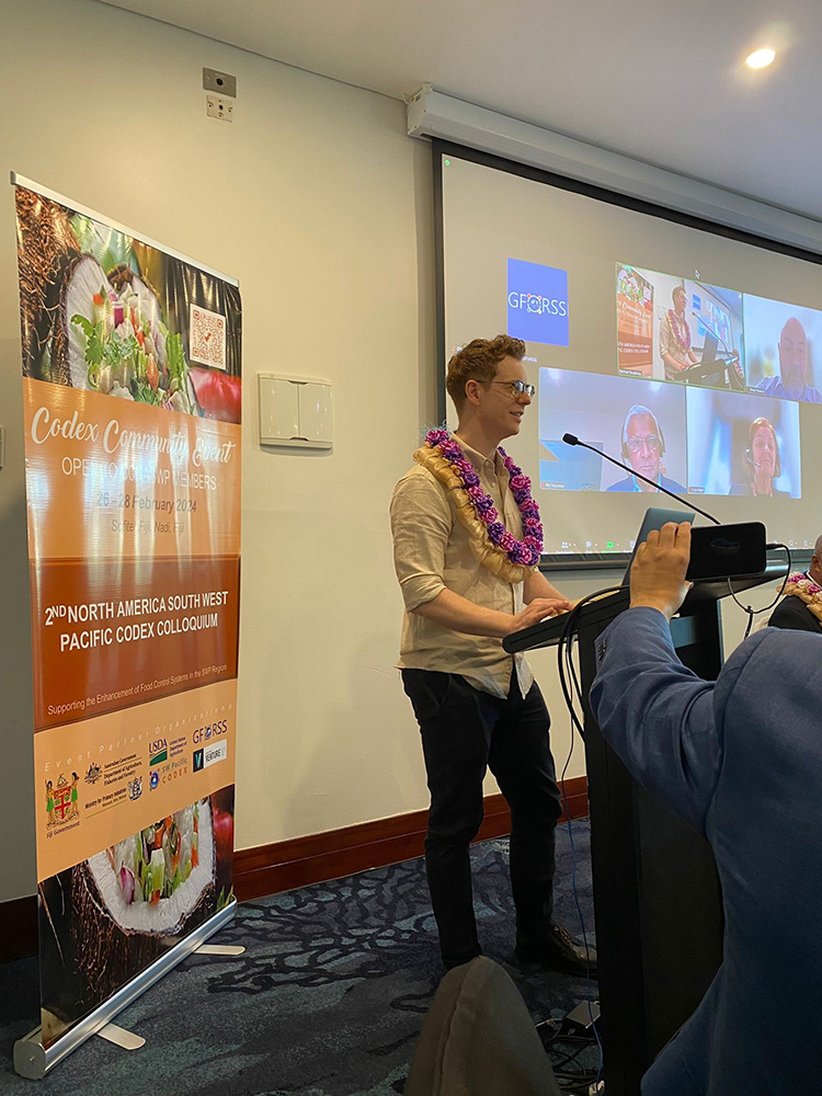 Image of a person standing at a podium, in front of a presentation at the 2nd CCNASWP colloquium. They are Scott Mersch, Director, Codex Australia, Australian Department of Agriculture, Fisheries and Forestry.