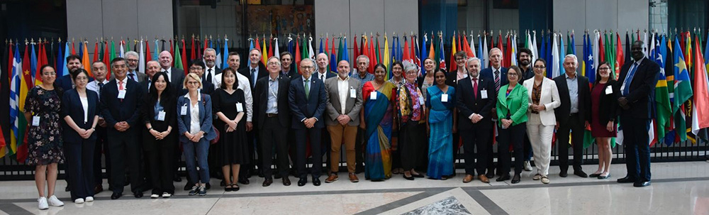 Image of a large group of people standing in front of a row of flags, including Gabrielle Vivian-Smith and Sophie Peterson - they are at the SPG meeting of the IPPC in Rome