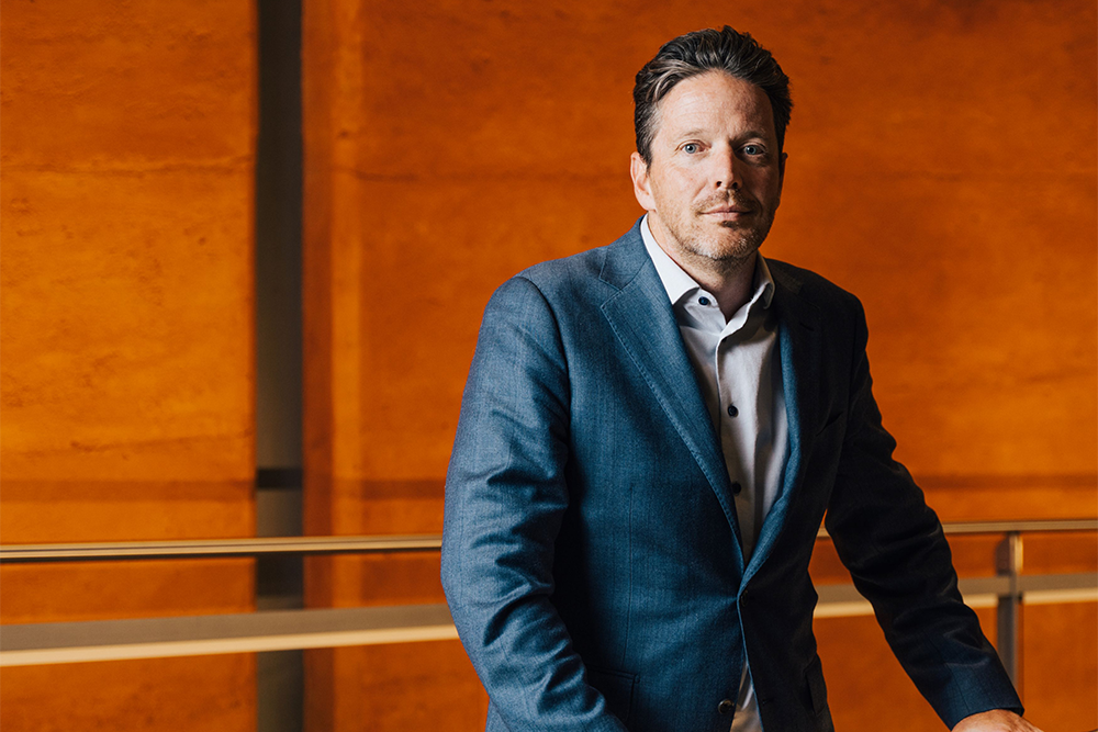 Image of a person in a suit standing in front of an orange backdrop