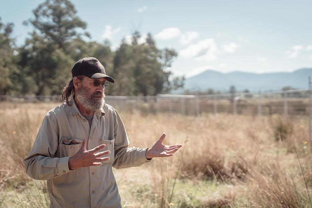 Uncle Dave Wandin standing in a field of dry grasses and trees and mountains in the background