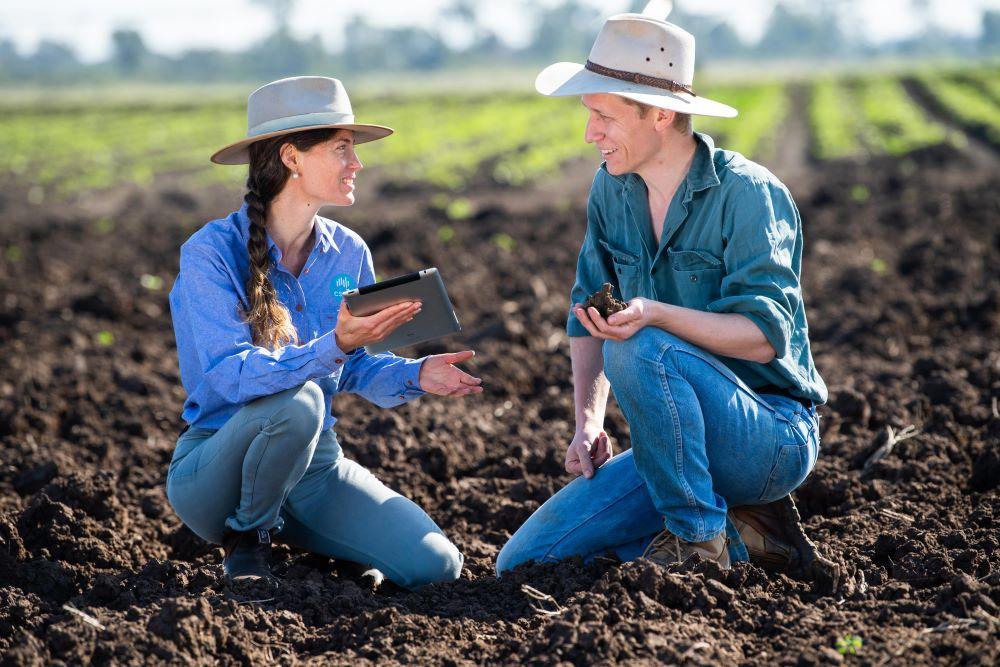 Image of two people sitting in a field with dark soil