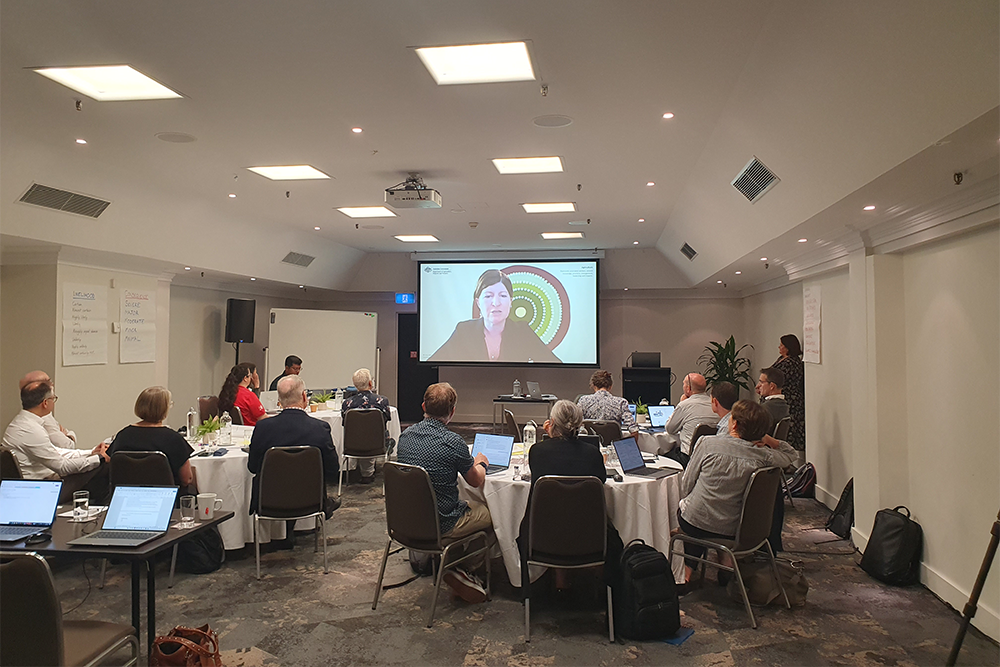 Image of a group of people sitting in a room, watching a presentation on a screen