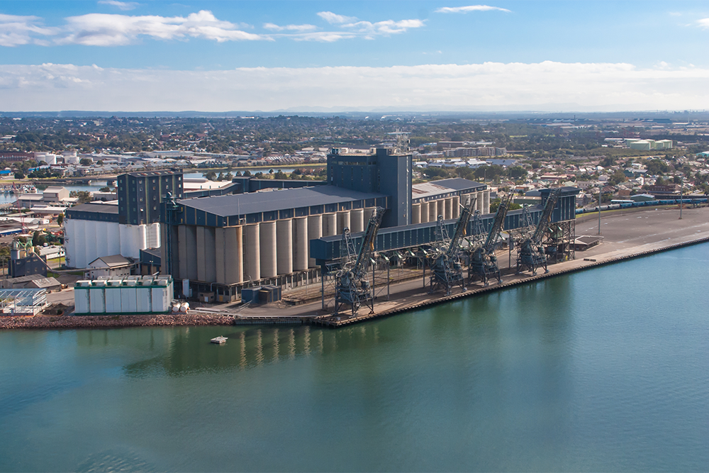 Image of a large building on a body of water, with multiple silos and cranes