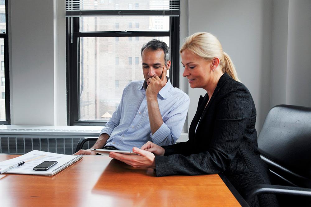 Image of two people sitting in an office, looking at an electronic tablet