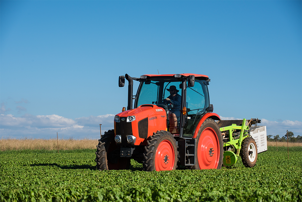 Image of an orange and black tractor in the middle of a field of green crops