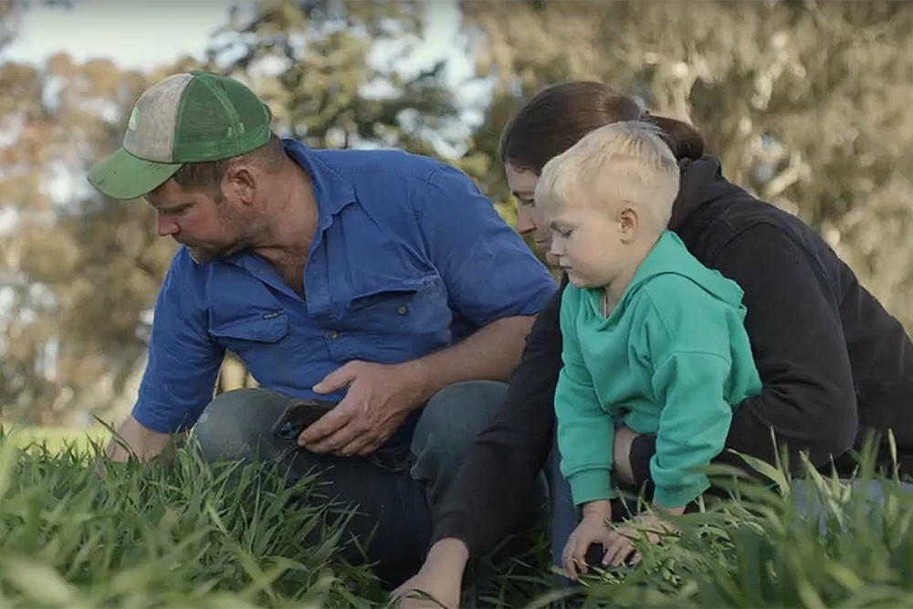 Image of two adults and a child sitting on grass out in a paddock