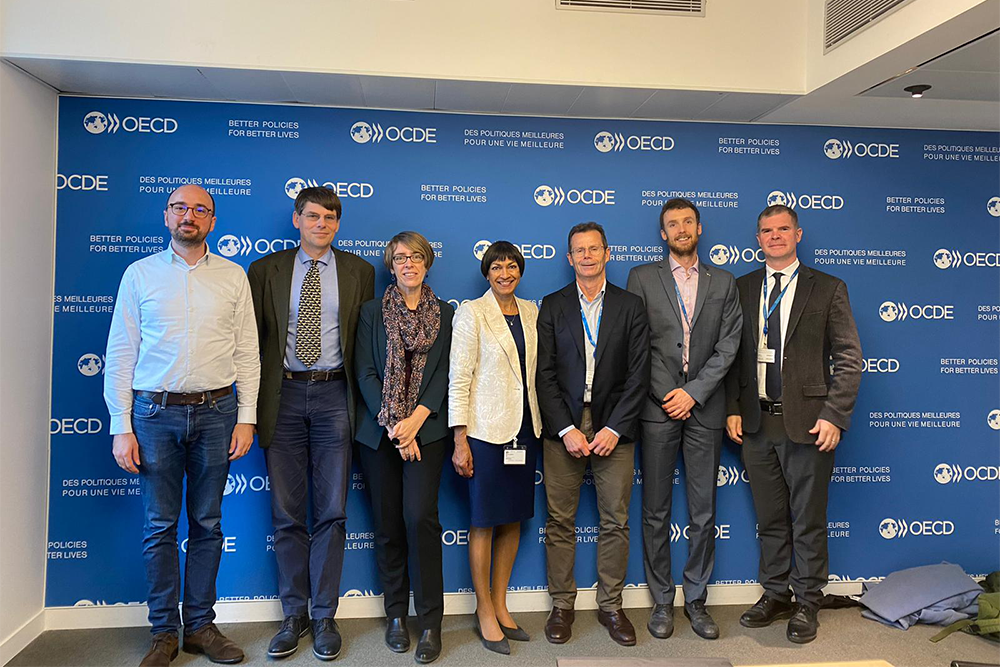 Image of a group of 7 people standing in front of an event banner wall