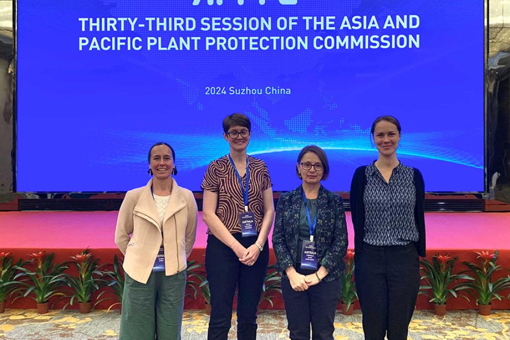 Image of four people standing in front of large screen which says Thirty-third session of the Asia and Pacific Plant Protection Commission