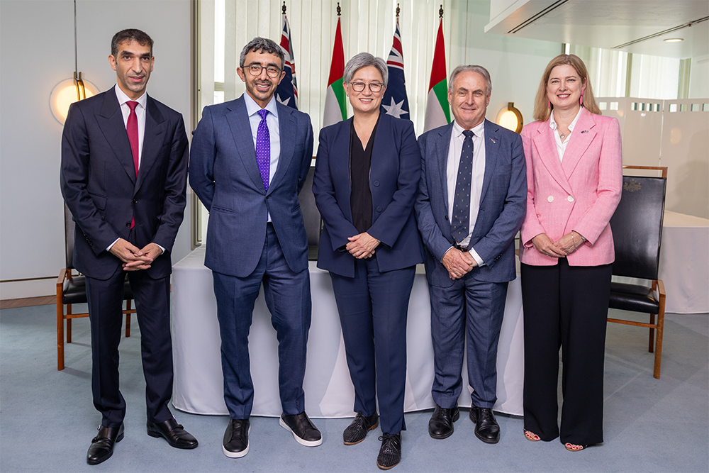 Image of 5 people standing in a line in front of various national flags